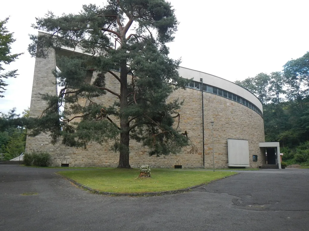 Katholische Pfarrkirche St. Pius, Rundbau aus ineinandergreifenden Raumschalen mit indirekt belichtenden Glasfronten und Lichtbändern zum flach geneigtem Pultdach, Schalbeton mit Sandsteinverkleidung, Hans Schädel, 1960 über Fundamenten von 1914/15, oktogonaler Kapellenanbau als Betonskelettanbau mit bemalten Glasflächenfenstern, 1962; mit Ausstattung, Sankt-Pius-Straße 25, AktenNr. D-6-76-121-34