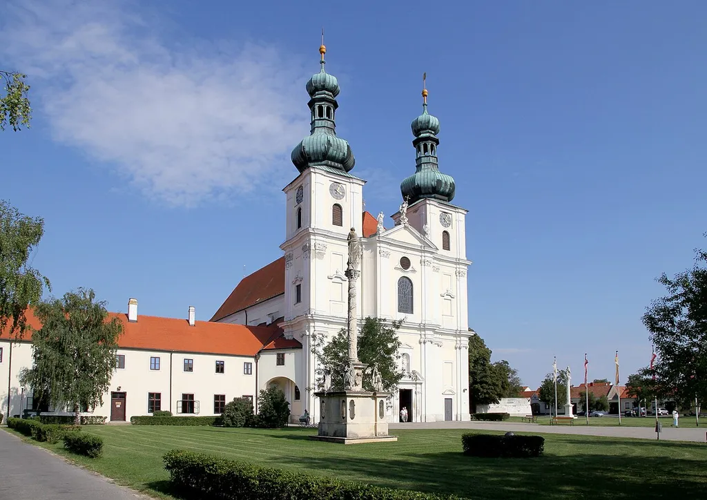 Die Basilika Mariä Geburt in der burgenländischen Stadt Frauenkirchen. Im Vordergrund die Mariensäule und links ein Gebäude des Franziskanerklosters.