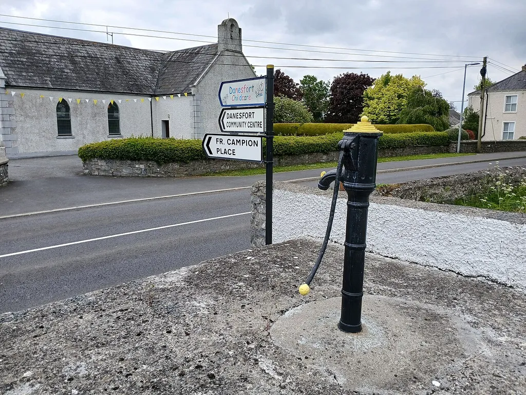 Roadside pump in Danesfort, painted in the Kilkenny colours. St Michael's Church is in the background.