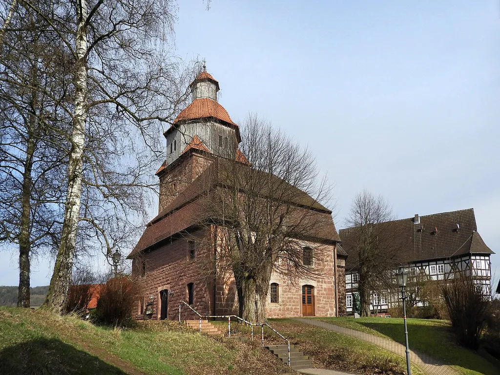 Der erhöht stehende, die Ortssilhouette prägende, wuchtige Turm der Bischhäuser Kirche befand sich einst im Zentrum einer mittelalterlichen Burganlage. Der die Kirche umgebende zentrale Platz wurde im Rahmen der Dorferneuerung 1997 umgestaltet. Die Linde, die in 1936 als Naturdenkmal ausgewiesen wurde, steht auf der Südseite des Platzes, in Gesellschaft mit weiteren alten Bäumen. Wegen seiner künstlerischen, geschichtlichen und städtebaulichen Bedeutung ist die Kirche ein geschütztes Kulturdenkmal.