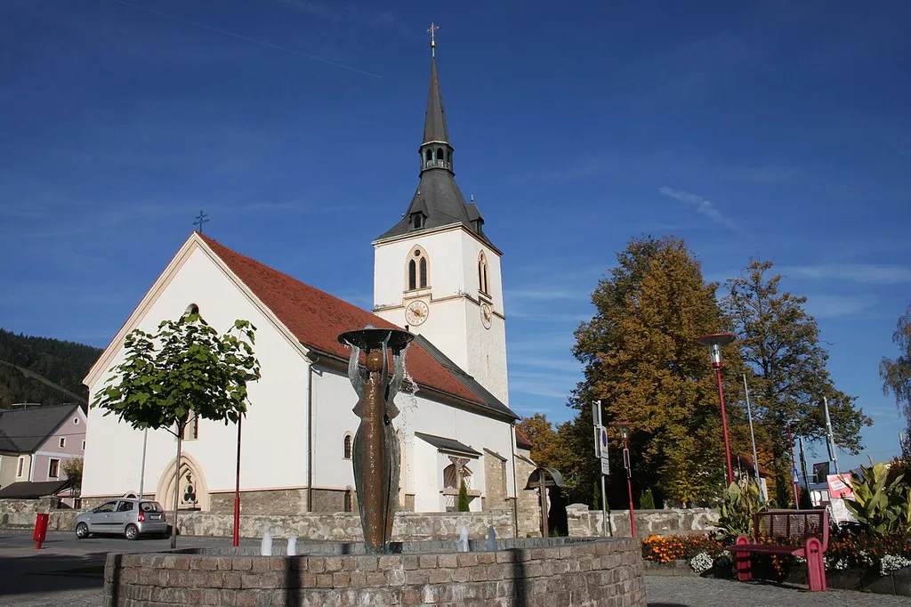Fohnsdorf, Hauptplatz, Kirche, Brunnen mit mittiger Statue weiblich eine Schale überkopf tragend, Künstler zum Brunnen nicht genannt This media shows the protected monument with ObjektID 56599 in Austria. (Commons, de, Wikidata)