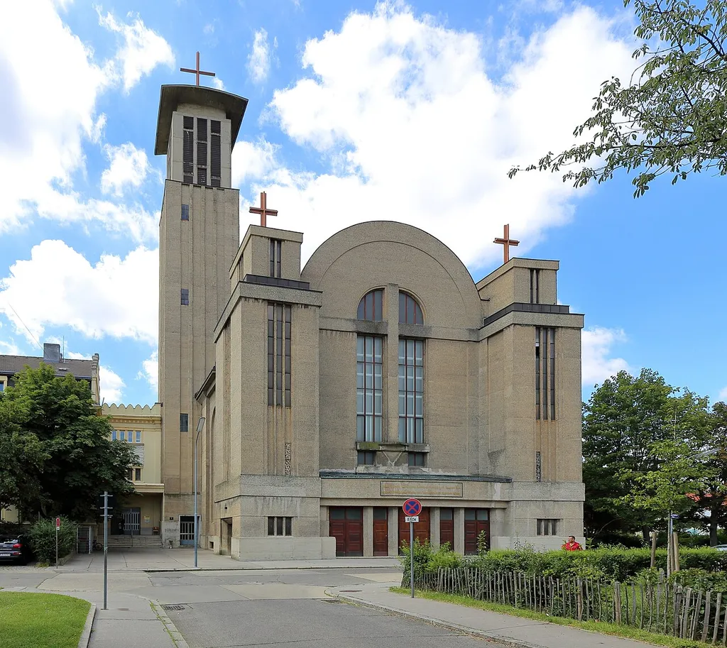 Nordansicht bzw. Hauptfassade der ehemaligen Kloster- und Pfarrkirche Maria vom Berge Karmel (Karmeliterkirche) am Stefan-Fadinger-Platz 1 im 10. Wiener Gemeindebezirk Favoriten.Die Kirche wurde ab 1928 anstelle einer abgebrannten Notkirche nach Plänen von Hans Prutscher errichtet und erst 1942 vollendet. Sie war nach Plecniks wegweisender Pfarrkirche auf der Schmelz (1911) die zweite „Betonkirche“ in Wien. Am 21. Februar 1945 wurde sie durch Fliegerbomben weitgehend zerstört (mit 140 Todesopfern). Nach Kriegsende erfolgte der Wiederaufbau, so dass nach der Wiederherstellung von Kuppel und Dach (1950) die Unterkirche 1951 geweiht werden konnte. Die ab 1957 begonnene Wiederherstellung der Oberkirche und der Bau des Turmes erfolgte stark verändert nach Plänen von Helene Koller-Buchwieser und mit der Glockenweihe am 15.Mai 1966 wurde der Wiederaufbau abgeschlossen. Mit Jahresende 2014 erfolgte die Übergabe des Gotteshauses mit Klostergebäude und Garten mangels Gläubiger, Priestermangel und Kostenreduktion, etc. an die aufstrebende syrisch-orthodoxe Metropolie.