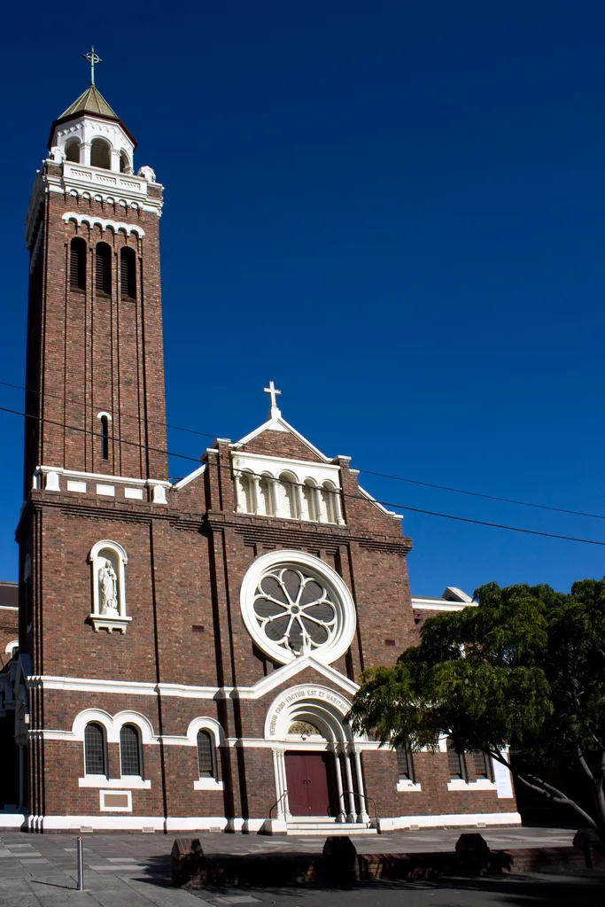St John's Church, the second church within the St John's complex, was built in 1900 to the design of architects McCrae and O'Toole. It is an idiosyncratic interpretation of the Romanesque style, built in red brick. The main facade is asymmetrical and incorporates a 10 metre high Celtic cross, pressed terracotta panels in the gable with representation of the stars of the Southern Cross, and a 26 metre high round tower with conical roof. The cross is of Stawell stone and weighs 21 tons. It portrays the head of Christ at its centre, surrounded by the four evangelists in full-relief. Below are full-length bas-relief portraits of St John and St Patrick. The remainder of the cross is carved with Celtic runes. The designer of the cross is not known.