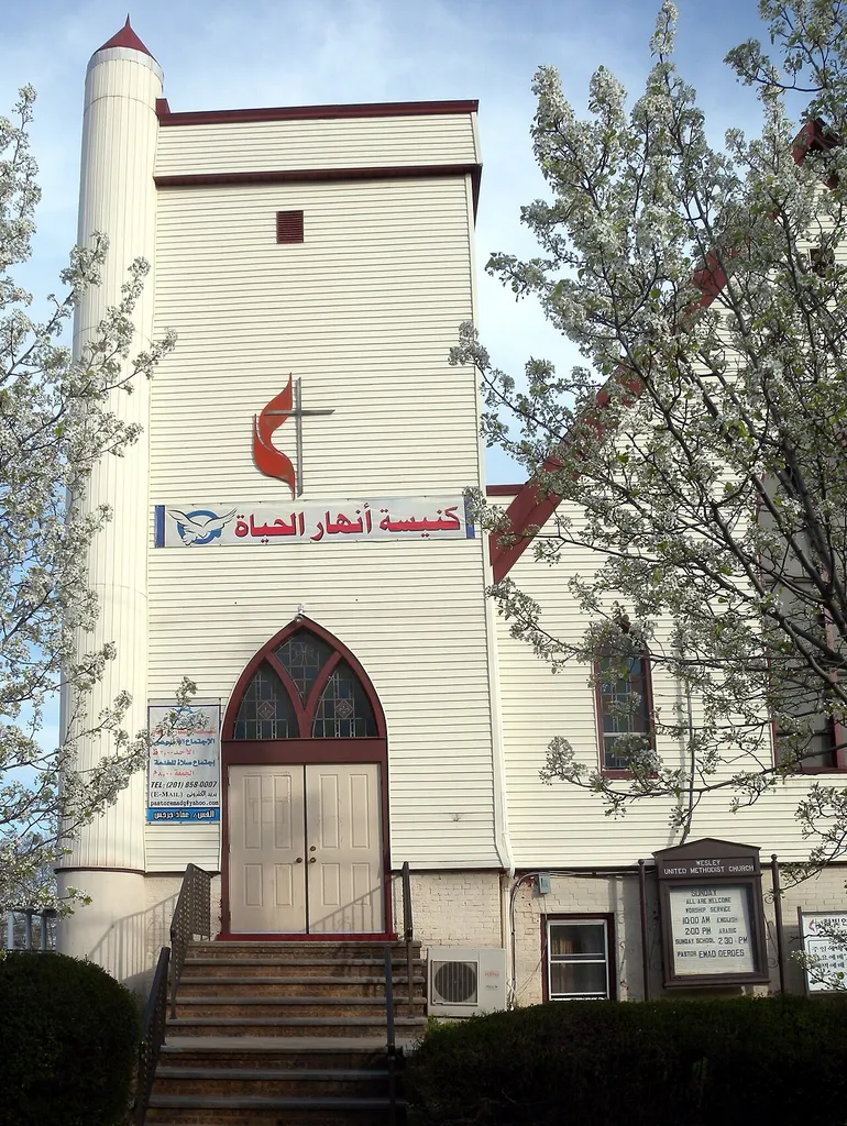 Looking east from Avenue C at steeple of Wesley United Methodist Church, with Arabic inscription, on a sunny afternoon.