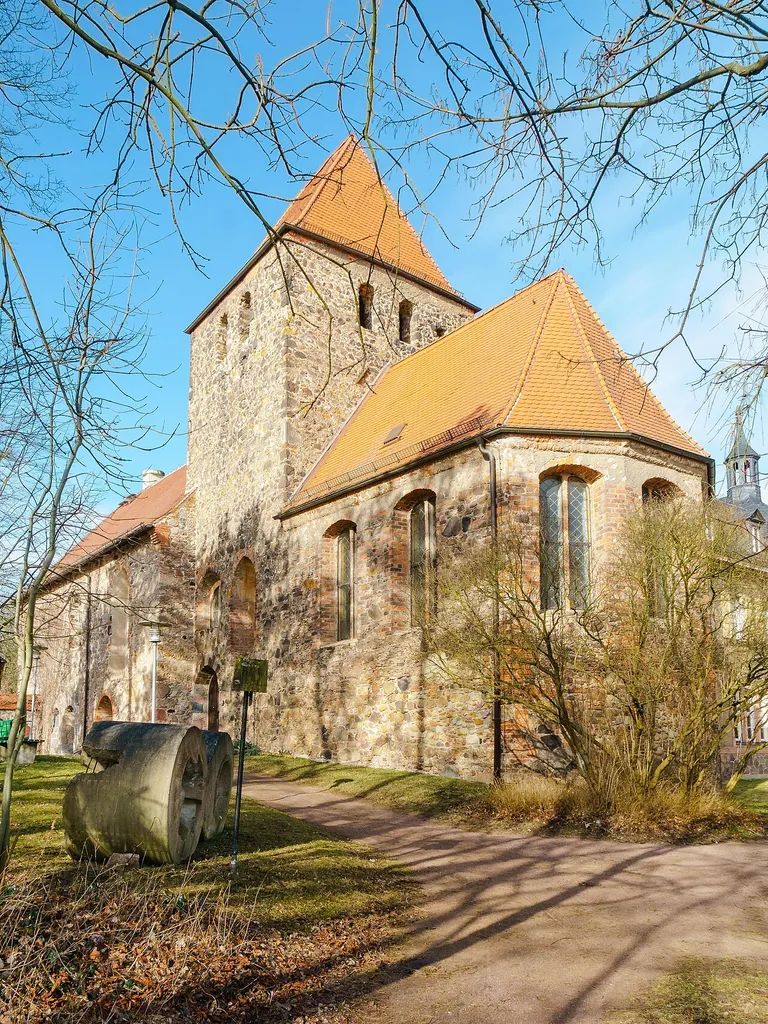 Kirche in Muldenstein. Im Vordergrund zwei Mahlsteine aus der Papierfabrik Muldenstein