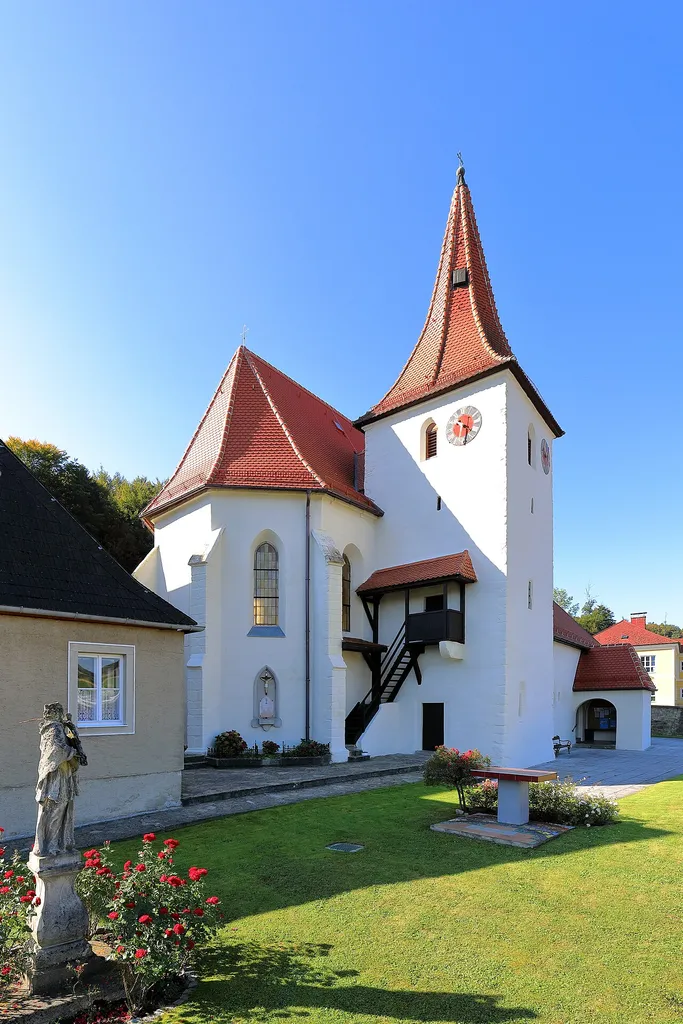 Der Kirchturm mit dem Chor der röm.-kath. Pfarrkirche hll. Simon und Judas Thaddäus in der niederösterreichischen Marktgemeinde Altlengbach. Im Vordergrund der ehemalige Friedhof und ein Bildstock des hl. Nepomuk aus der Mitte des 18. Jahrhunderts.