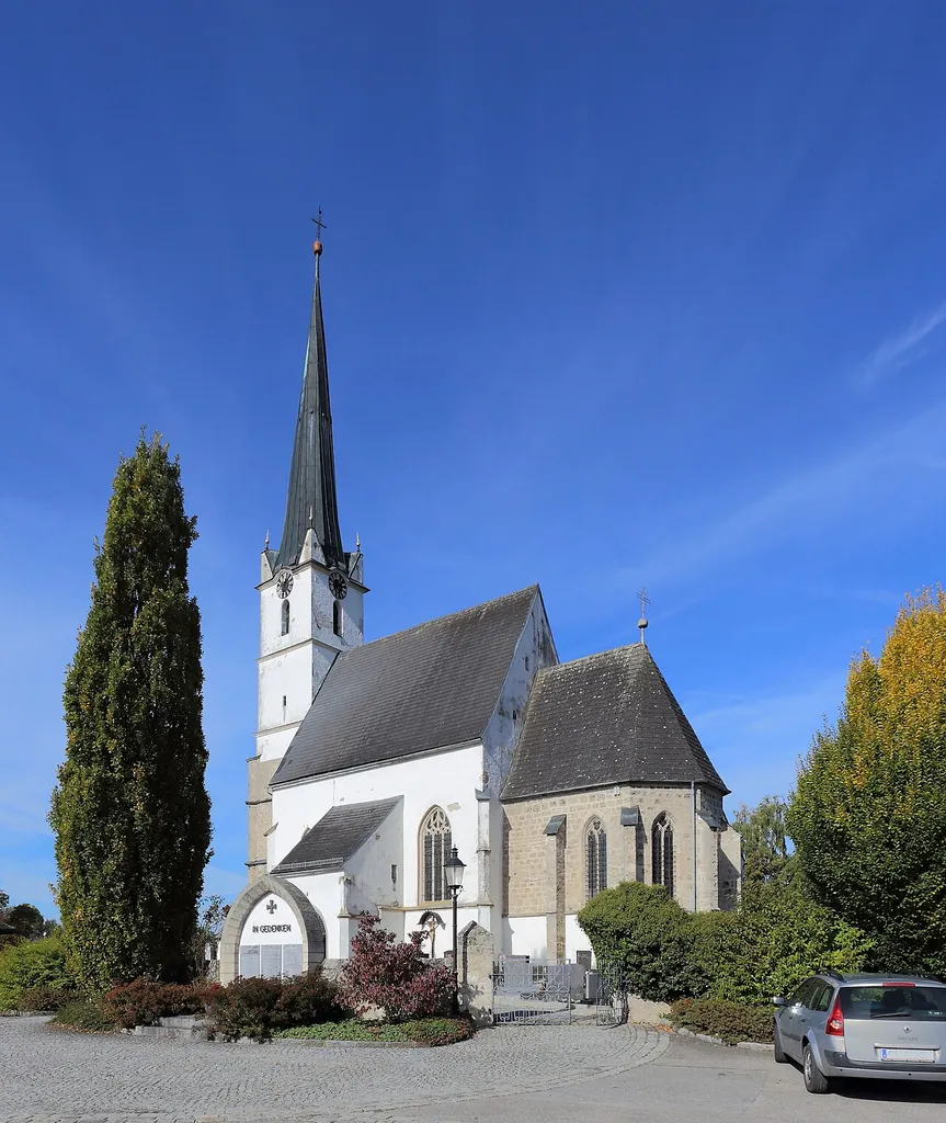 Südostansicht der katholischen Pfarrkirche Mariä Himmelfahrt in der oberösterreichischen Gemeinde Mühlheim am Inn. Ein gotischer Sakralbau um 1500 mit einem Westturm, einem einschiffigen, dreijochigen Langhaus und einem eingezogenen, niedrigeren Chor.