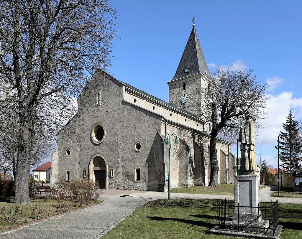 Südwestansicht der röm.-kath. Pfarrkirche hl. Laurentius in der niederösterreichischen Marktgemeinde Sollenau und rechts im Vordergrund eine barocke Nepomukstatue aus dem Jahr 1732.Die Kirche wurde ursprünglich im 12. Jahrhundert in Form einer niedrigen, dreischiffigen Basilika errichtet und Ende des 15. Jahrhunderts zu einer Staffelkirche umgebaut. Der Kirchturm wurde ab der Mitte des 13. Jahrhunderts im Osten angebaut und im 14. Jahrhundert um ein Wehrgeschoß sowie im 15. Jahrhundert um ein Glockengeschoß erhöht.