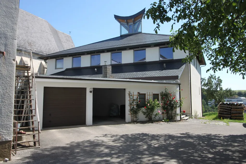 Neue Pfarrkirche Kirchham, Westfassade, vorgestellten Erschließungtrakt der Kirche unter einem Pultdach, davor Garagen eines Verbindungstraktes zur Tischlerei
