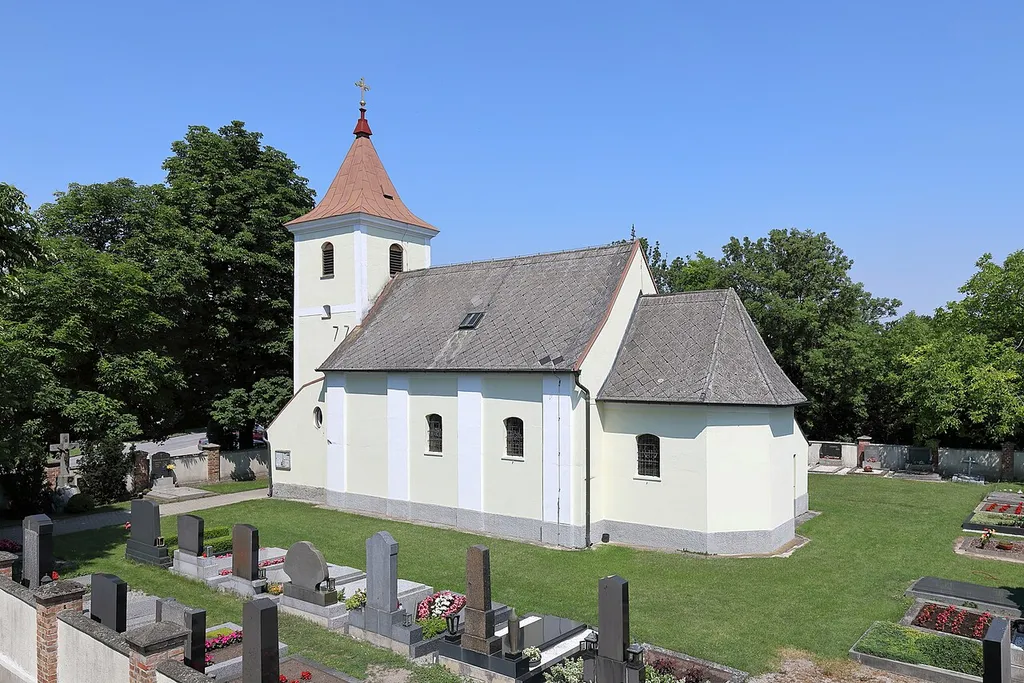 Südostansicht der röm.-kath. Filialkirche hl. Dreifaltigkeit in Wagram an der Donau, ein Dorf in der niederösterreichischen Marktgemeinde Eckartsau. Die kleine spätbarocke Dorfkirche mit einem gedrungenen vorgesetzten Westturm wurde in der 2. Hälfte des 18. Jahrhunderts errichtet.