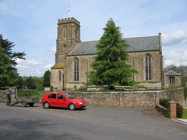 St. Margarets, Corsley. A view looking north to the church of St. Margaret of Antioch at Corsley. The gentleman is loading a mower onto the trailer after cutting the grass within the graveyard to the left and behind the photographer's position.