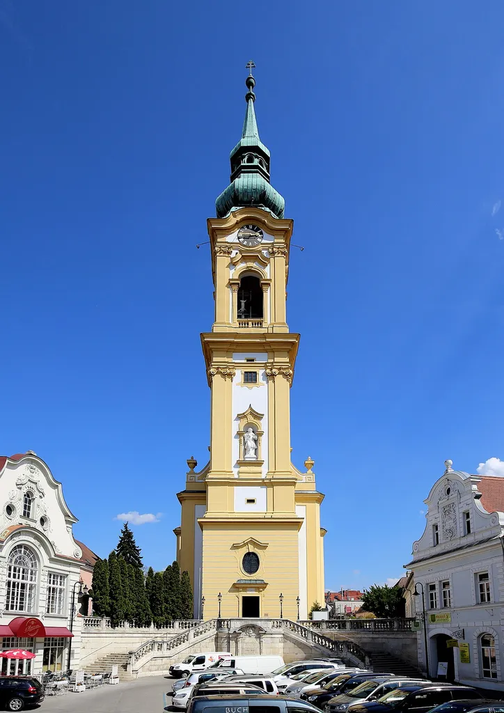 Westansicht der katholischen Stadtpfarrkirche hl. Stephan in der niederösterreichischen Stadt Stockerau. Eine spätbarocke-frühklassizistische Saalkirche auf einem Hügel inmitten der Altstadt. Der vorgestellte und stadtbildbeherrschende Westturm wurde von 1722 bis 1725 von dem Baumeister Franz Jänggl errichtet und ist mit 88 Meter der höchste Kirchturm Niederösterreichs. 1777/78 erfolgte der Abbruch des gotischen Langhauses und anschließend der Neubau durch den Wiener Baumeister Peter Mollner.