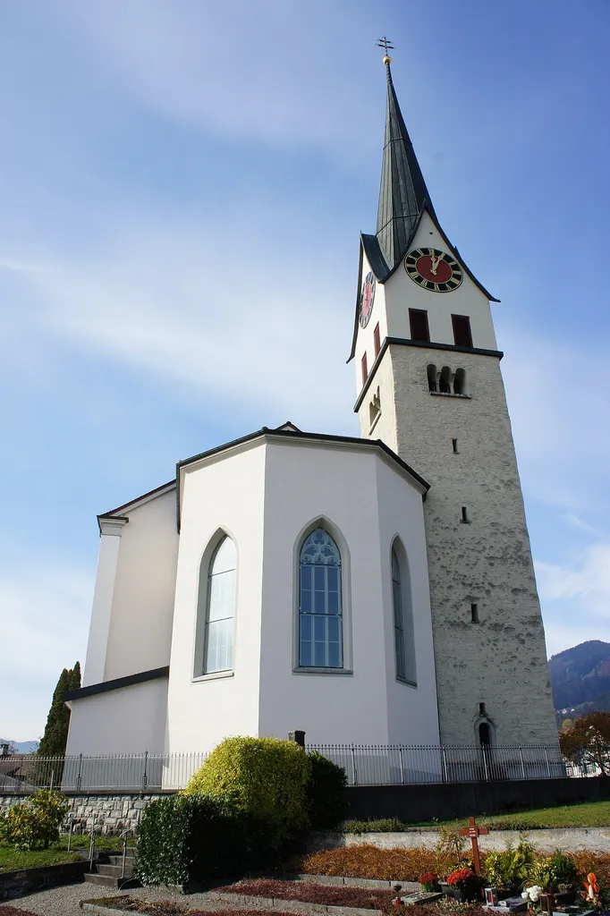 Blick aus Osten auf die kath. Kirche in Marbach. Rechts von der Apsis steht der Kirchturm, der im Gegensatz zur Kirche im unteren Teil nicht verputzt ist. Im Vordergrund ein Teil des Friedhofes.