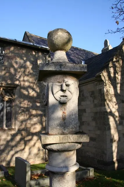 Part of a sundial in St Peter's parish churchyard, Thorpe Salvin, South Yorkshire. It has alternating smiling and frowning faces on its four sides. The sundial is probably 18th century, but it is set on a plinth dated 1841.
