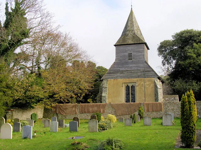 St Mary and St Peter Church, Wilmington This view shows the west of the church with its shingled spire with wooden facings. The large hessian sheets had been hung over the church wall to dry by a local craftsman who was making a flint wall nearby.