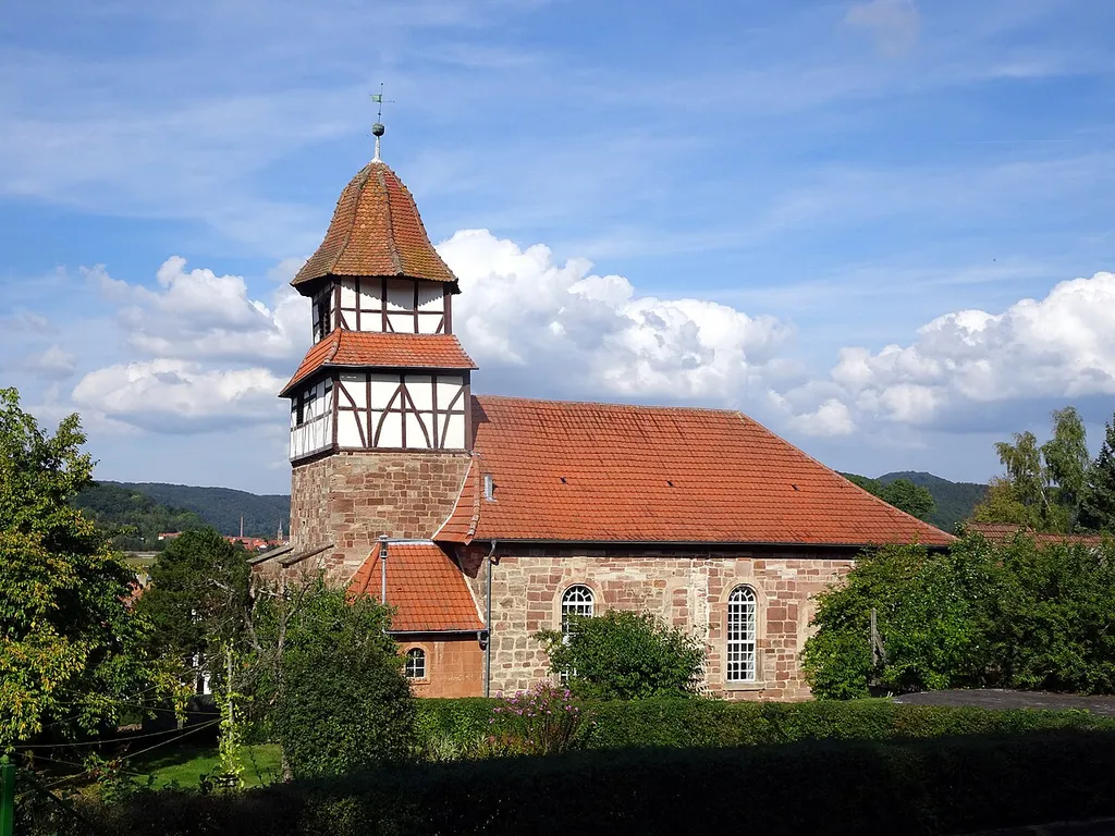 Die Evangelische Kirche in Aue. Aue ist ein Ortsteil von Wanfried im nordhessischen Werra-Meißner-Kreis. Text von G. Gress an der evangelischen Kirche: "Diese Kirche stammt vermutlich aus dem 12. Jahrhundert. Sie war dem heutigen Heiligen Clemens geweiht. Von dem romanischen Baustil ist der untere Teil des Turmes mit Westeingang noch erhalten geblieben. 1719 verstärkte man den Turm durch Stützpfeiler. Das Kirchenschiff wurde 1831 abgebrochen und durch ein weit größeres ersetzt. 1894 erfolgte eine Innenrenovierung, Bänke sowie Kanzel und Altarverkleidung wurden erneuert. 1912 wurde das Helmdach des Turmes ausgebessert. In dem Turmknopf fand man mehrere Urkunden, die älteste stammte aus dem Jahre 1719, eine andere aus 1846. Rund um die Kirche lag der Friedhof, der 1851 geschlossen wurde. Die alte Begräbnisstätte der Gutsherren des Adels von Aue und von Eschwege soll sich unter dem Altar befinden. Es ist nicht ausgeschlossen, dass die Kirche ursprünglich auch als Wehrkirche diente. Der Kirchhof war mit einer Mauer umgeben, so dass die Einwohner dort Schutz fanden, wenn kriegerische Horden durch das Werratal zogen. 1527 wurde in Aue die Reformation eingeführt. Der letzte katholische Pfarrer war Johannes Leinbach. Seit der Reformation hatte Aue keine eigene Pfarrei. Im 30jährigen Krieg blieb die Kirche verschont, da der ansässige Adel Schutzbriefe von Wallenstein erworben hatte." Aue liegt am Werratal-Radweg.
