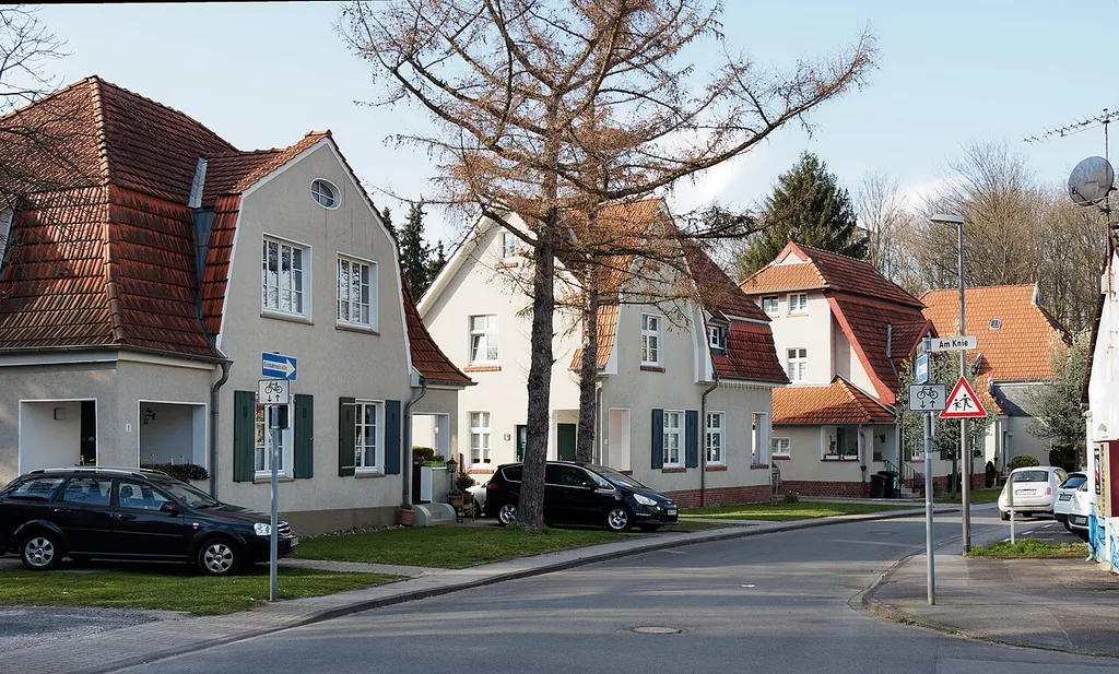 Wohnhäuser der Bergarbeitersiedlung Teutoburgia der ehemaligen Zeche Teutoburgia, Straßen Schadeburgstraße, Am Knie in Herne-Holthausen. Hinter den Bäumen befindet sich das Fördergerüst (Schacht 1) der ehemaligen Zeche.