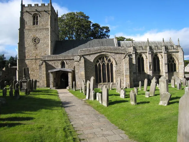 Gravestones in Romaldkirk church This photograph shows the paved stone path leading up to the entrance to Romaldkirk church. On either side of the path there is an interesting collection of gravestones basking in the late-afternoon sunshine. The clock on the church tower shows the time at which this photograph was taken.
