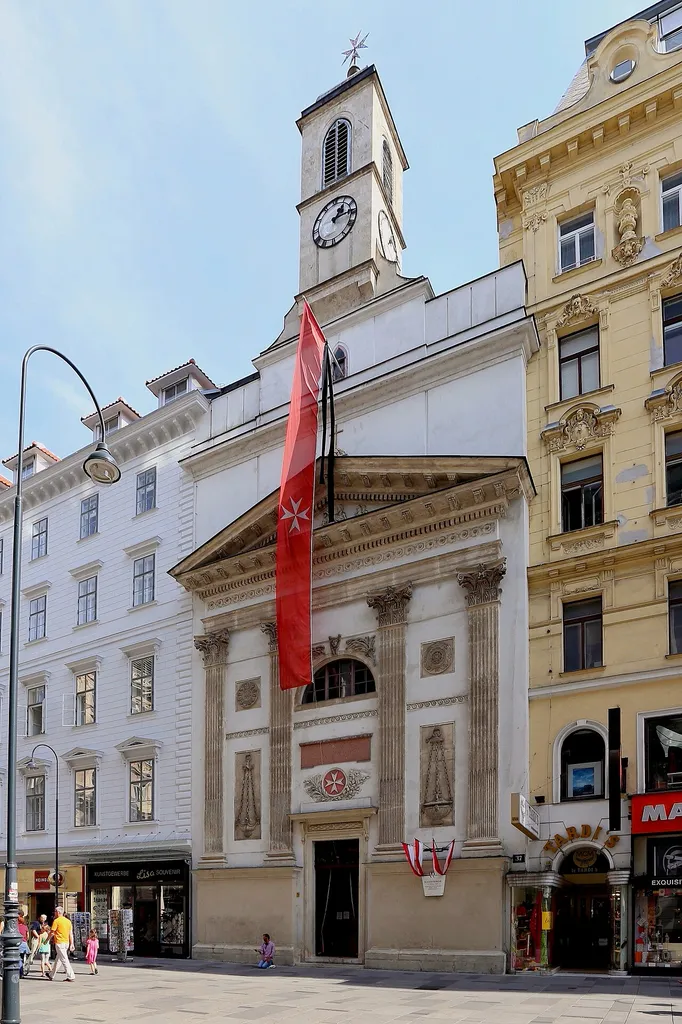 Die Malteserkirche in der Kärntner Straße in Wien mit einem osteuropäischen Bettlertouristen davor. Der einschiffige Sakralbau wurde Mitte des 15. Jahrhunderts errichtet. Zur Barockzeit wurde die Kirche dem Zeitgeschmack entsprechend umgebaut. Eine weitere Umgestaltung erfolgte Anfang des 19. Jahrhunderts. Dabei erhielt die Kirche eine Fassade im Empirestil mit korinthischen Pilastern und einem kleinen Turm. Die Inneneinrichtung wurde ebenfalls teilweise neu gestaltet wie beispielsweise die Kanzel.