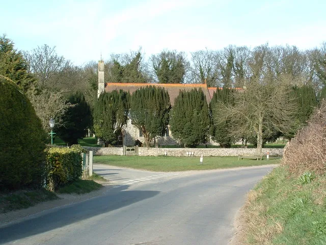 View north along part of Shernborne Road, Shernborne, Norfolk, with the parish church of SS Peter and Paul hidden behind a row of yew trees