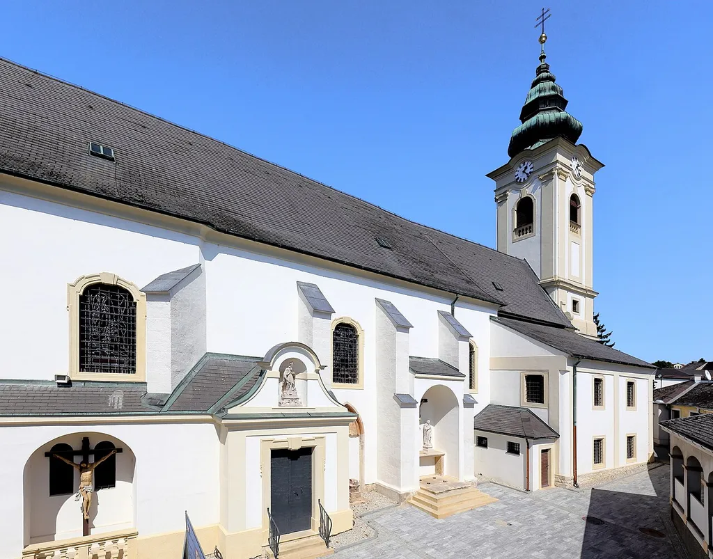 Südwestansicht der röm.-kath. Pfarrkirche hll. Nikolaus und Gallus in der burgenländischen Bezirkshauptstadt Neusiedl am See.Die Kirche wurde im 15. Jahrhundert in erhöhter Lage errichtet und im Laufe der Jahre mehrfach erweitert bzw. umgebaut. Der jetzige Kirchturm mit dem Zwiebelhelm wurde 1737 errichtet, nachdem der Vorgängerturm desolat war und einstürzte.