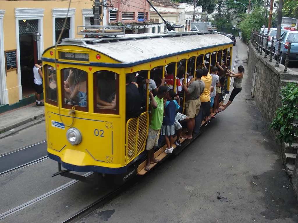 Heavily loaded (or "packed") tramcar 02 of Rio de Janeiro's Santa Teresa tramway just a few meters east of Largo do Guimarães junction, inbound from Paula Matos or the carhouse. (Contrary to the sign showing on the rear of the tram, "Dois Irmãos", car 02 cannot have been coming from Dois Irmãos, because the track used by trams inbound from Dois Irmãos at this location runs along the parallel street at upper right (where cars are parked), at a slightly higher level.)