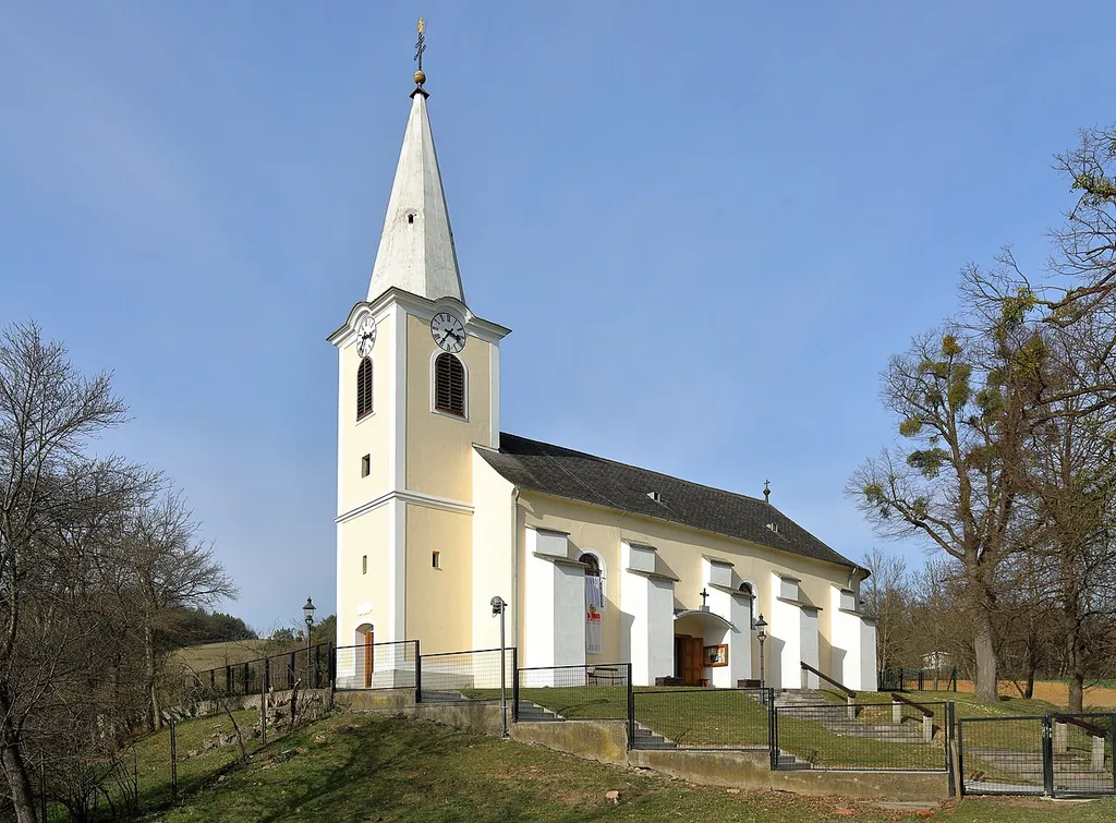 Südwestansicht der röm.-kath. Pfarrkirche hl. Petrus und Paulus in Unterrabnitz, ein Ortsteil der burgenländischen Gemeinde Unterrabnitz-Schwendgraben. Der einfache Bau mit Westturm und halbrundem Chor wurde anstelle einer Vorgängerkirche 1772 errichtet und ist von einem Friedhof umgeben.