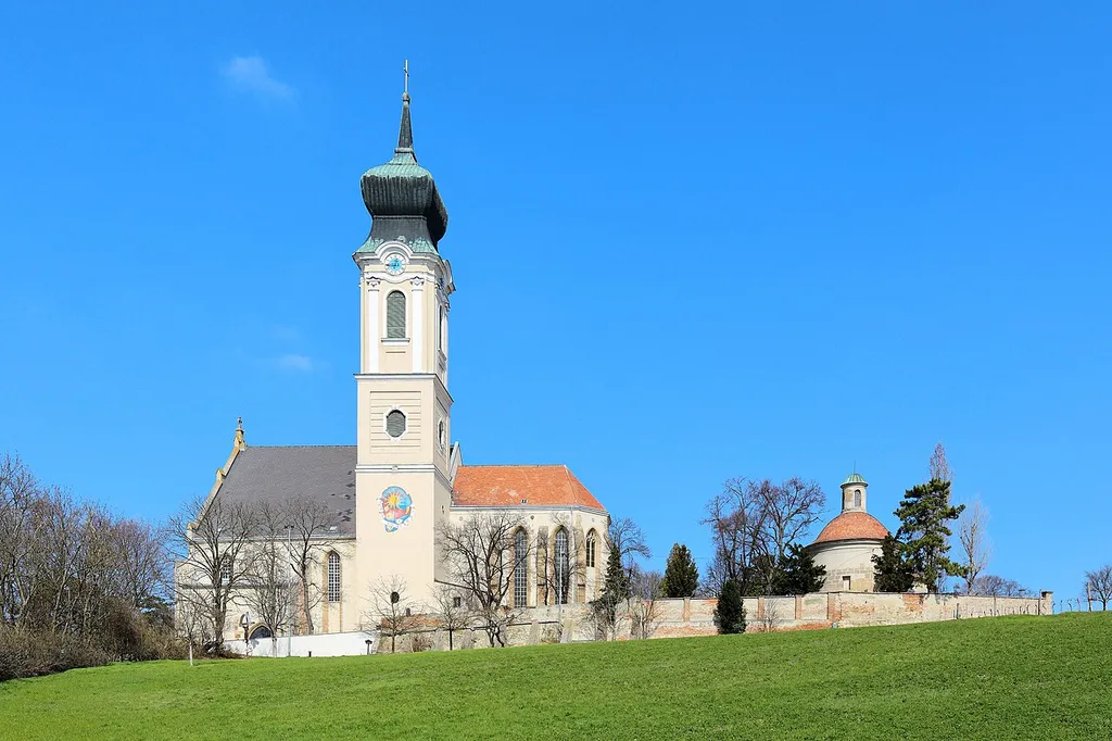 Südansicht der römisch-katholischen Pfarrkirche hl. Martin in der niederösterreichischen Bezirkshaupstadt Mistelbach mit Friedhofsmauer und dem ehemaligen Karner.Die spätgotische Hallenkirche mit eingezogenem Chor und einem in den Obergeschossen barockisierten Südturm wurde östlich des Ortes auf einem Plateau errichtet. Südöstlich der Kirche befindet sich ein schlichter romanischer Karner mit halbkreisförmiger Apsis aus dem Anfang des 13. Jahrhunderts. Der Karner wurde 1719 barockisiert und wird heute als Kapelle hl. Katharina genutzt.