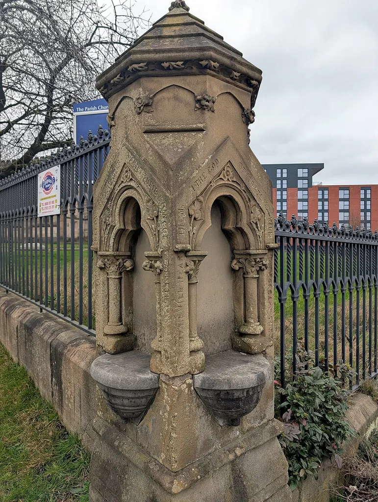 St Thomas's, Pendleton, old drinking fountain, from the southeast. Both sides are visible. The fountain is stopped up with concrete. Around the edges of the sides of the fountain is inscribed "JEHOVAH WILL HEAR THEM / I THE GOD / OF ISRAEL / WILL / NOT FORSAKE THEM / WHEN THE POOR AND NEEDY / SEEK WATER / AND THEIR / TONGUE FAILETH FOR THIRST" (Isaiah 47:17)