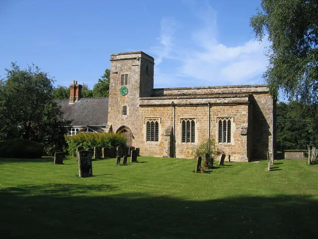 Church of England parish church of St James, Nether Worton, Oxfordshire. Notice the small figure carved into the right hand end of the tower lintel. Beneath it is a stone inscribed "Roberte Parsons 1630". The house on the left was built as the parish school.