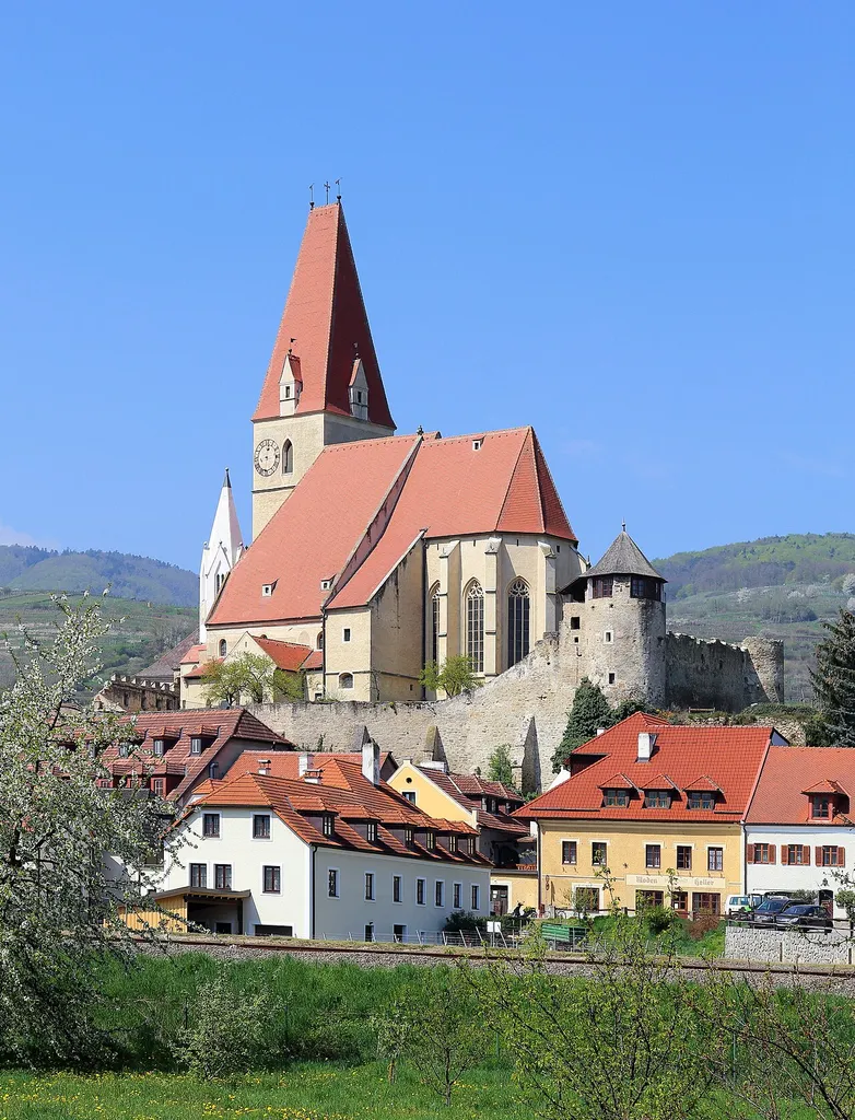 Südostansicht der römisch-katholischen Pfarrkirche Mariae Himmelfahrt in der niederösterreichischen Marktgemeinde Weißenkirchen in der Wachau.Die dominierend den Ort überragende Pfarrkirche ist ein wuchtiger, vielteiliger Bau, der in mehreren Bauphasen zwischen dem 13. und 18. Jahrhundert errichtet wurde und von einer turmbewehrten Befestigungsanlage umgeben ist. Der spätgotische Chor wurde von 1519 bis 1526 errichtet und der mächtigte Nordwestturm 1502. Der kleinere Turm - südlich in der Westfront leicht eingestellte - ist der ursprüngliche Turm der zweischiffige Vorgängerkirche und wurde um 1330 errichtet.