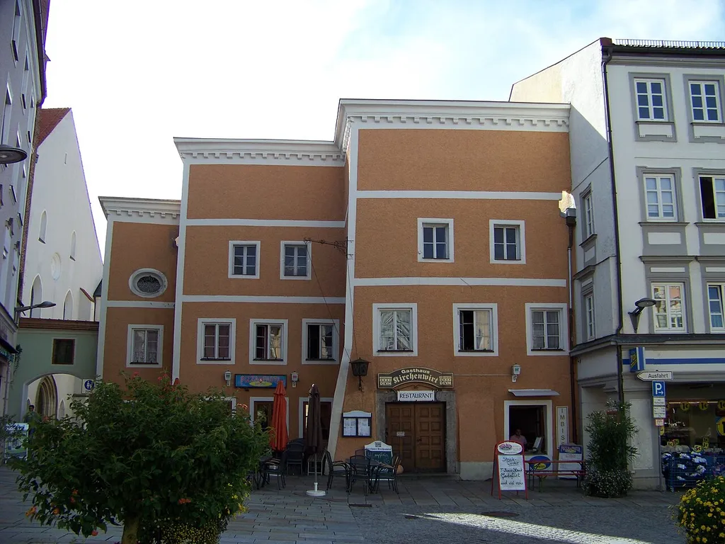 Pfarrkirchen, Stadtplatz 8. Kirchenwirt, dreigeschossiger Massivbau mit drei Rückstaffelungen im Grundriss am Durchgang zur Kirche, waagrechte Vorschussmauer, im Kern 16./17. Jahrhundert.