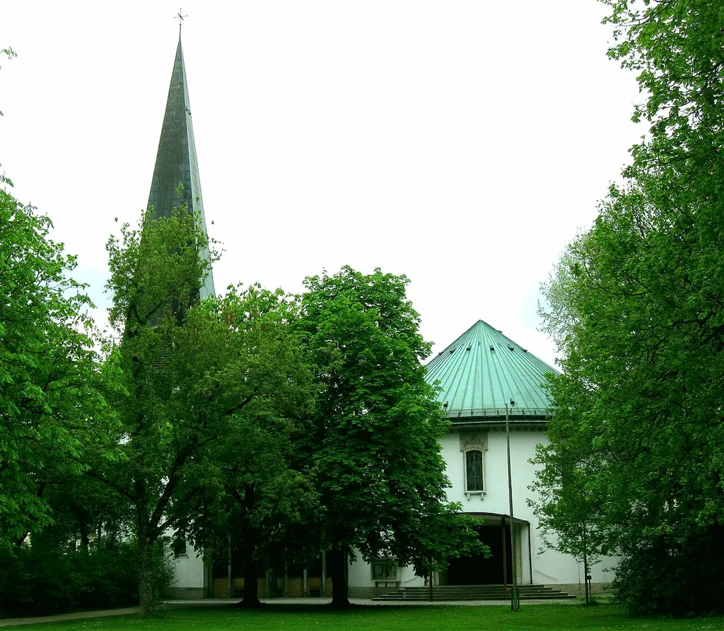 München; Maisinger Platz 22; Kath. Pfarrkirche St. Joachim, Kirchenraum über ovalem Grundriss, mit flacher Gewölbeschale, nierenförmig geschwungener Orgelempore und hohen Lamellenfenstern, 1955/56 von Franz Berberich und Oskar Haßlauer; Glockenturm mit hohem Spitzhelm, Eingang mit weit vorspringendem Dach; mit Ausstattung.