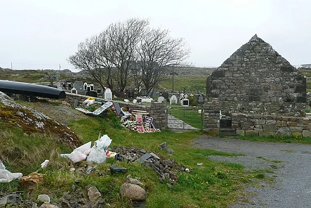 Burial ground at An Tra Bháin (Trawbaun) Like many, the church is derelict but the adjacent burial ground is still in regular use. There is a pile of discarded wreaths and commemorations behind the nearer wall.